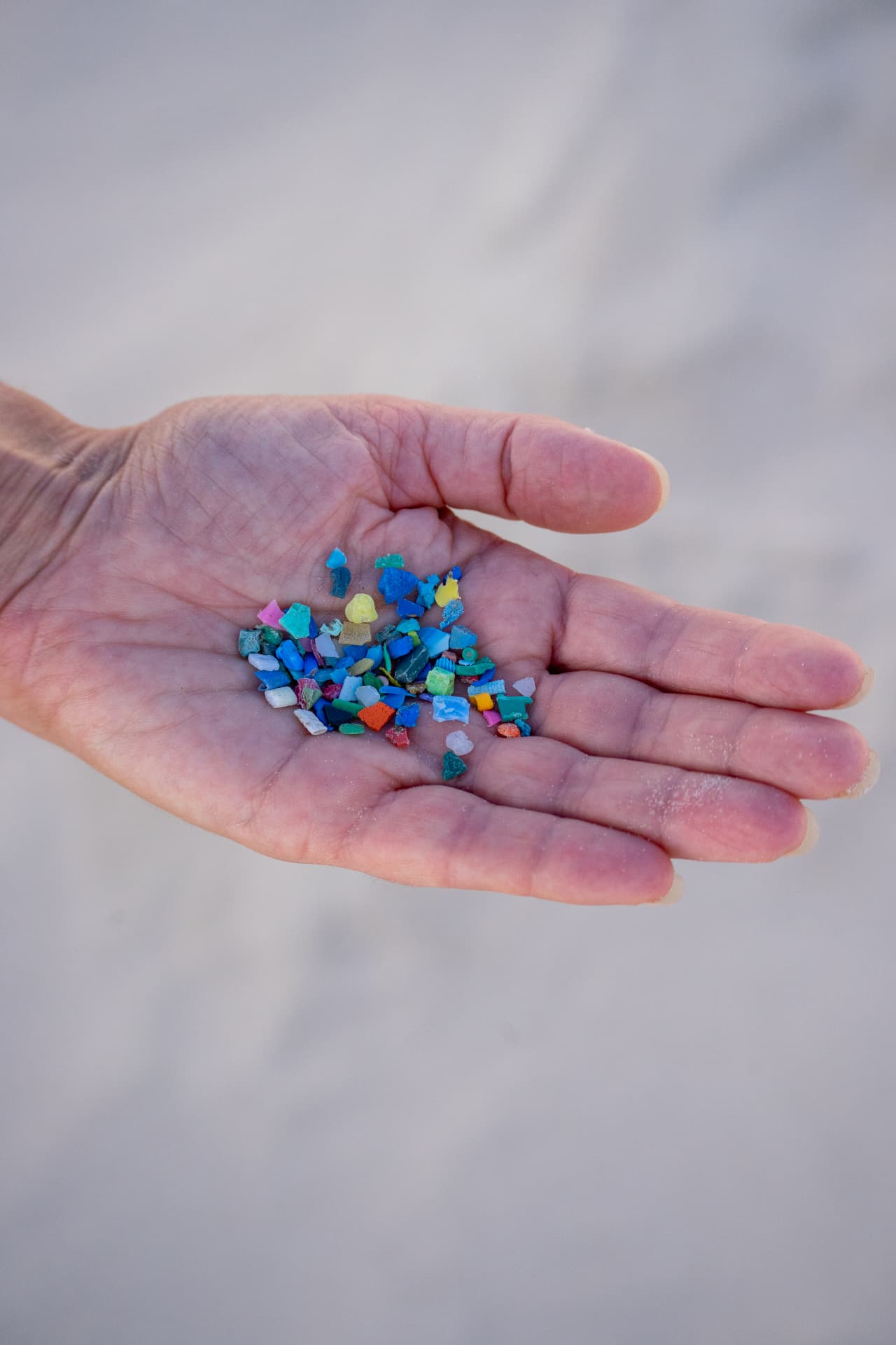 A hand holding small, colourful fragments of plastic - secondary microplastics that break off from larger items over time
