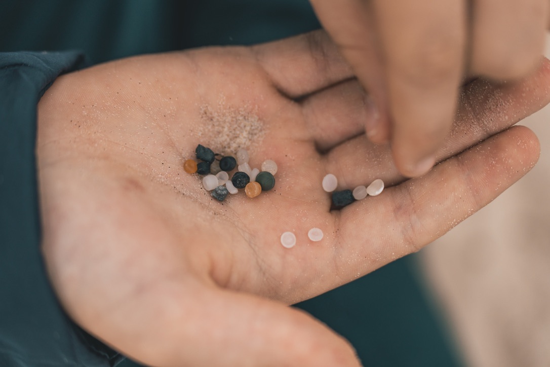 A small hand holding multicoloured plastic pellets and nurdles, examples of visible primary microplastic pollution.