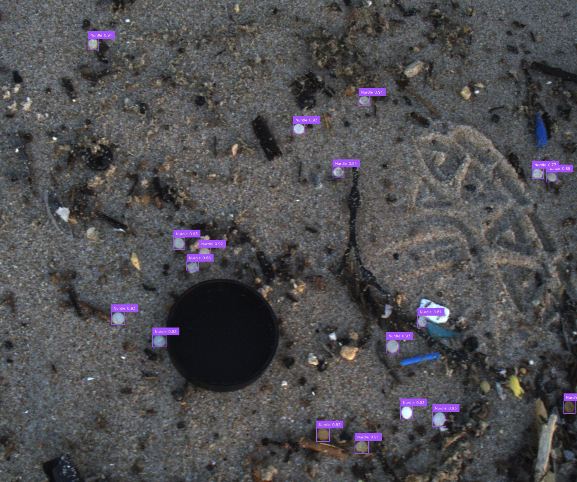 The same beach photograph with purple boxes and confidence scores marking each detected plastic pellet