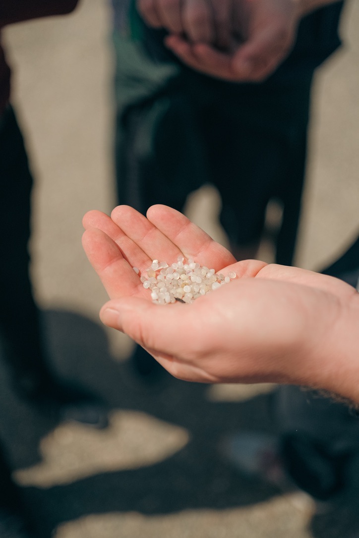 A hand holding clear plastic pellets, examples of primary microplastic pollution.